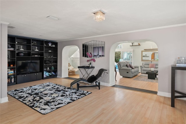 living room with wood finished floors, visible vents, ornamental molding, and arched walkways