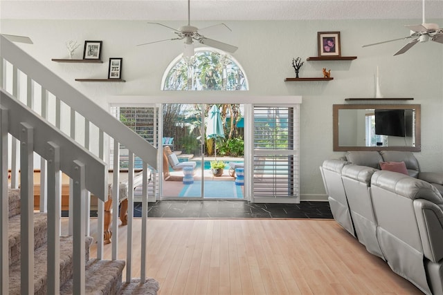 living room featuring wood finished floors, a ceiling fan, baseboards, and stairs