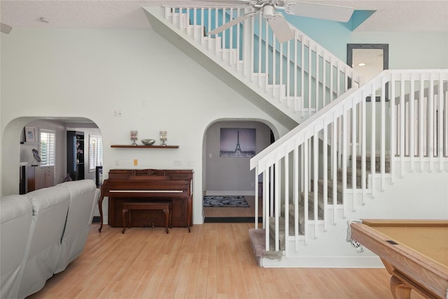staircase with a textured ceiling, wood-type flooring, arched walkways, a ceiling fan, and a high ceiling