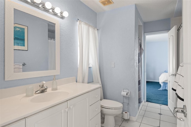ensuite bathroom featuring vanity, tile patterned floors, toilet, visible vents, and a textured wall