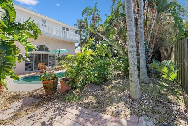 view of yard with fence, an outdoor pool, a patio area, and a balcony