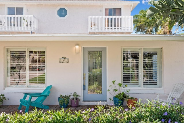 doorway to property featuring stucco siding, covered porch, and a balcony