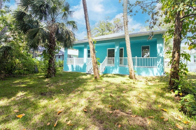 back of property featuring stucco siding, a lawn, and covered porch