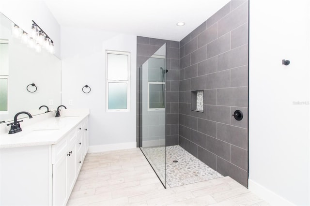 bathroom featuring walk in shower, baseboards, a sink, and double vanity