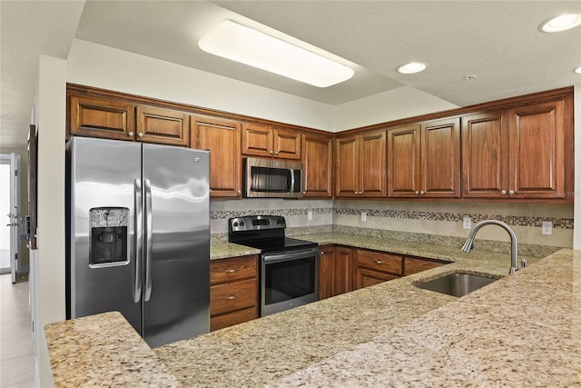 kitchen featuring light stone counters, brown cabinetry, stainless steel appliances, backsplash, and a sink