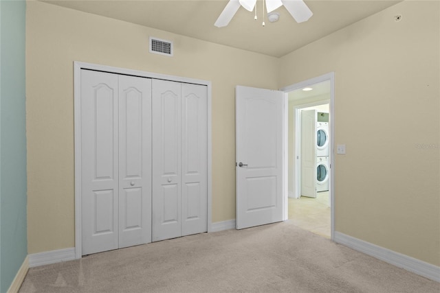 unfurnished bedroom featuring stacked washer / drying machine, visible vents, a closet, baseboards, and light carpet