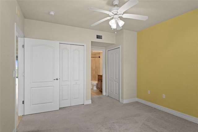 unfurnished bedroom featuring connected bathroom, visible vents, baseboards, light colored carpet, and multiple closets