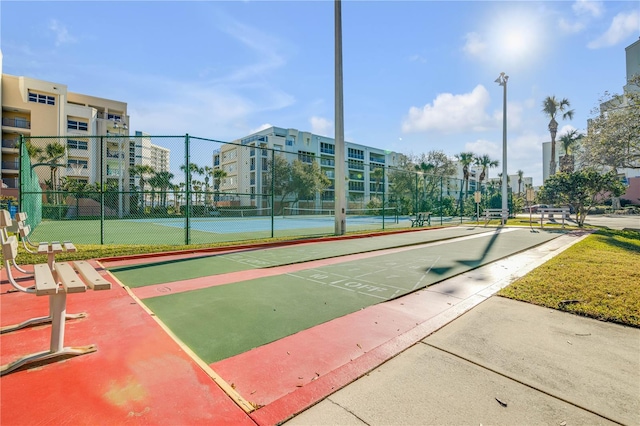 view of property's community featuring a tennis court, shuffleboard, and fence