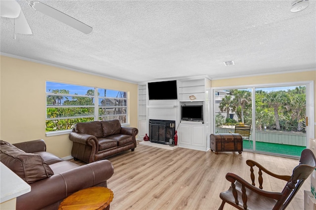 216 Dune Cir, New Smyrna Beach, FL 32169 - living area featuring a textured ceiling, crown molding, visible vents, light wood-style floors, and a glass covered fireplace