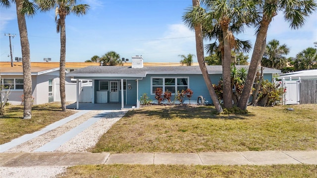 view of front facade with fence, a front lawn, dirt driveway, an attached carport, and a chimney