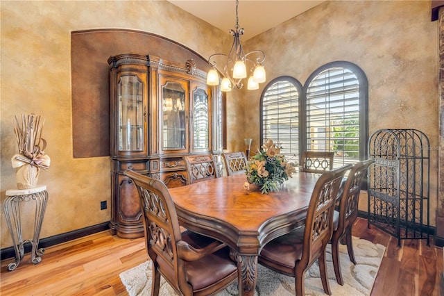 dining space featuring baseboards, a notable chandelier, a textured wall, and light wood-type flooring