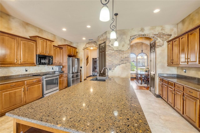 kitchen with a sink, brown cabinets, light stone counters, arched walkways, and stainless steel appliances