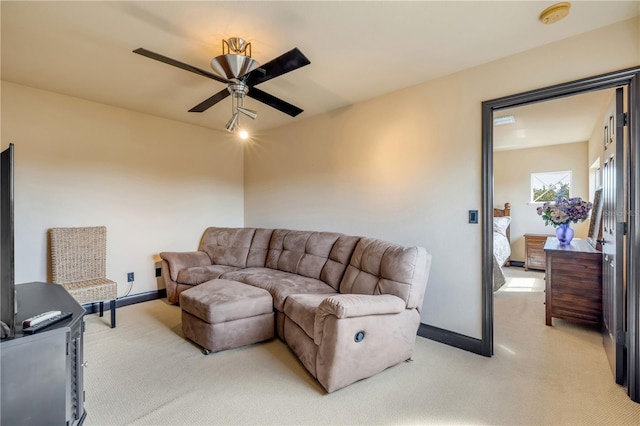 living area with baseboards, a ceiling fan, and light carpet