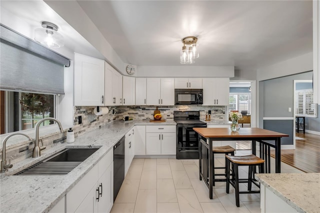 2548 E Compton St, Orlando, FL 32806 - kitchen with backsplash, a sink, light stone counters, white cabinets, and black appliances