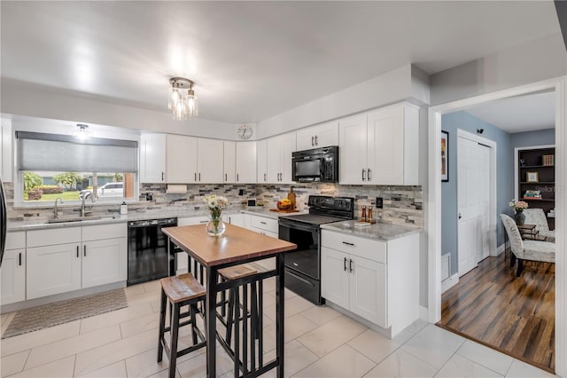 2548 E Compton St, Orlando, FL 32806 - kitchen with white cabinets, light stone countertops, a sink, decorative backsplash, and black appliances