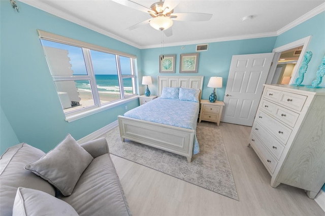 bedroom featuring crown molding, light wood-style flooring, baseboards, a water view, and visible vents