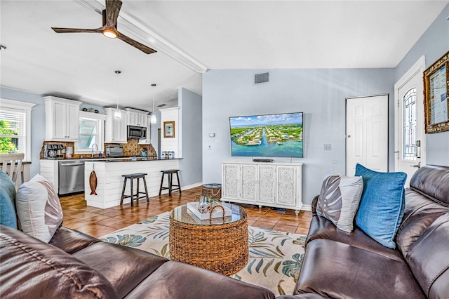 living room featuring ceiling fan, visible vents, light tile patterned floors, baseboards, and vaulted ceiling with beams