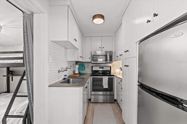 kitchen featuring appliances with stainless steel finishes, tasteful backsplash, a sink, light wood-style floors, and white cabinetry