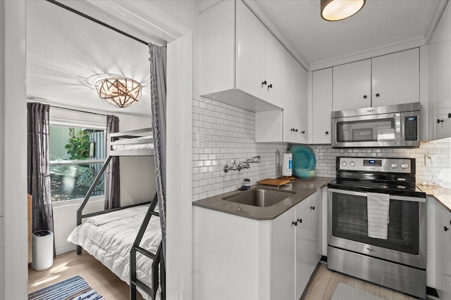kitchen with a sink, stainless steel appliances, light wood finished floors, and white cabinetry
