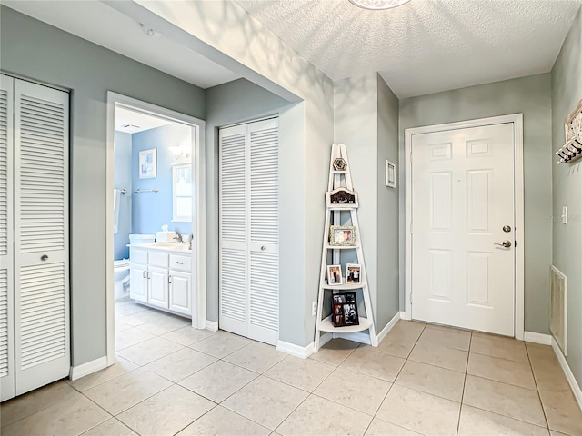 foyer featuring light tile patterned flooring, baseboards, and a textured ceiling