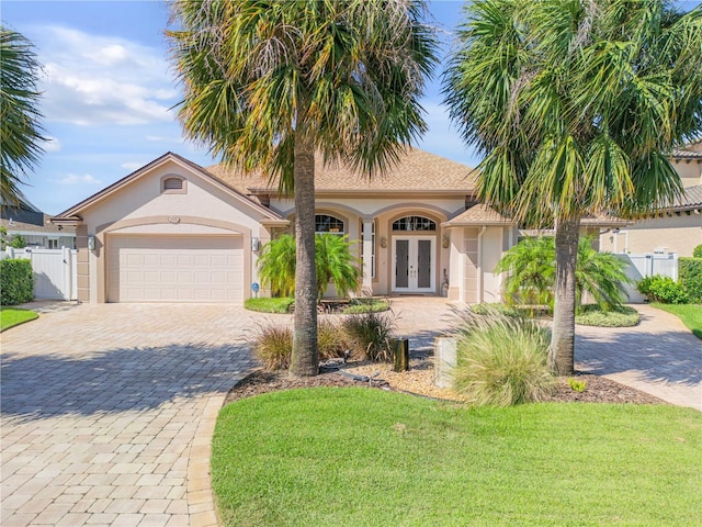 mediterranean / spanish home featuring french doors, a gate, decorative driveway, an attached garage, and stucco siding