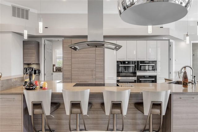 kitchen with visible vents, double oven, island range hood, white cabinets, and a sink