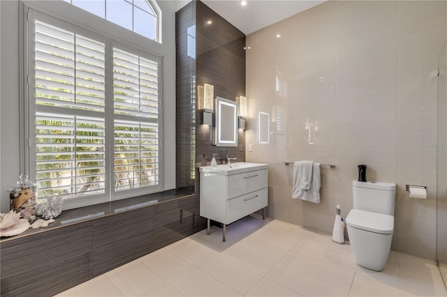 bathroom featuring tile patterned flooring, vanity, a towering ceiling, toilet, and tile walls