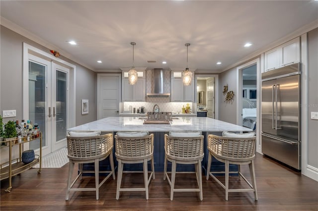 6771 Turtlemound Rd, New Smyrna Beach, FL 32169 - kitchen featuring a spacious island, wall chimney exhaust hood, decorative backsplash, light stone countertops, and built in fridge