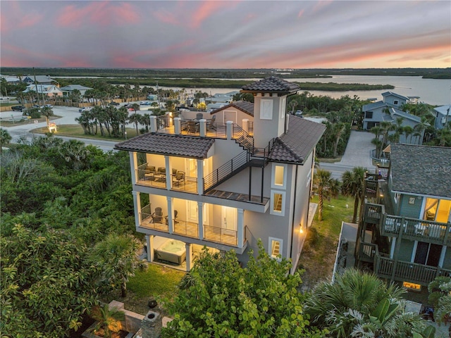 6771 Turtlemound Rd, New Smyrna Beach, FL 32169 - back of property at dusk featuring a tiled roof, stucco siding, a water view, and a balcony