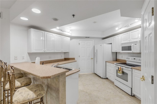 kitchen featuring white appliances, a sink, a raised ceiling, a breakfast bar, and a peninsula