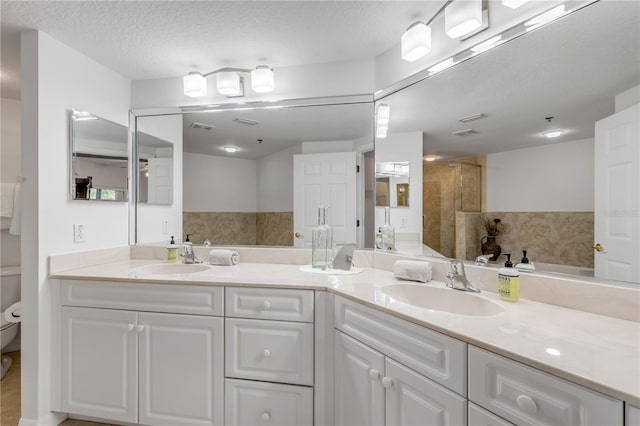 full bathroom with toilet, double vanity, tiled shower, and a textured ceiling