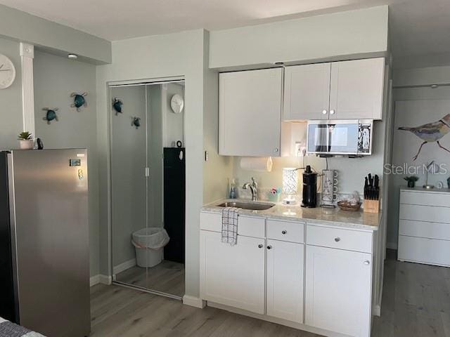 kitchen with light wood-style flooring, appliances with stainless steel finishes, a sink, and white cabinets