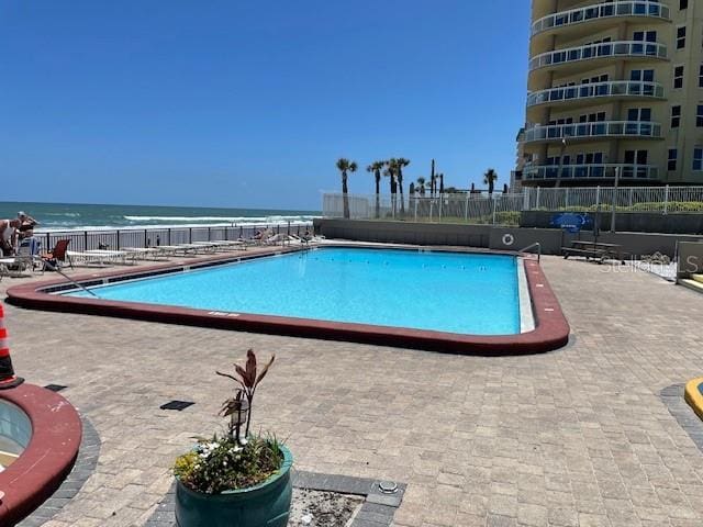 community pool featuring a water view, a patio area, and fence