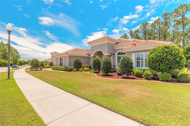 mediterranean / spanish house with a front lawn, stucco siding, and a tile roof
