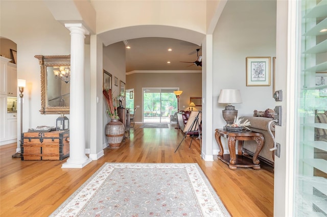 foyer entrance with decorative columns, ornamental molding, light wood finished floors, arched walkways, and a ceiling fan