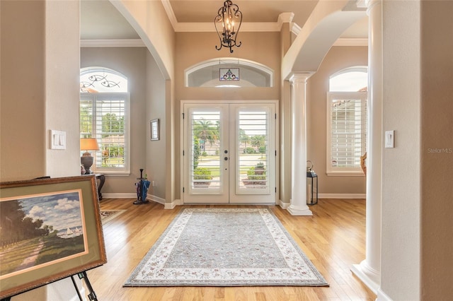 foyer entrance featuring ornamental molding, french doors, ornate columns, and light wood-style floors