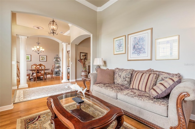 living room featuring wood finished floors, decorative columns, ornamental molding, an inviting chandelier, and arched walkways