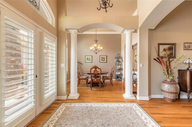foyer entrance featuring an inviting chandelier, decorative columns, baseboards, arched walkways, and light wood-style floors