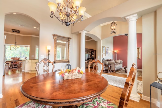 dining area with ceiling fan with notable chandelier, light wood-type flooring, ornate columns, crown molding, and arched walkways