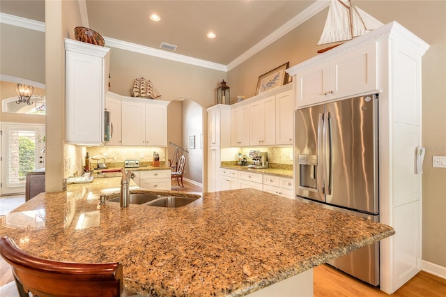 kitchen featuring a sink, a peninsula, crown molding, stainless steel fridge, and arched walkways