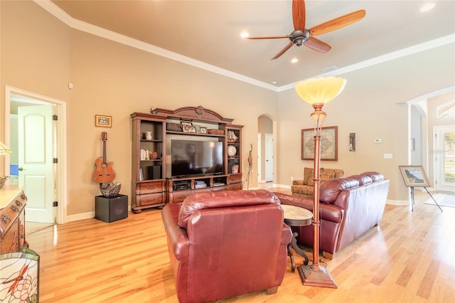 living area featuring light wood finished floors, crown molding, arched walkways, a ceiling fan, and baseboards