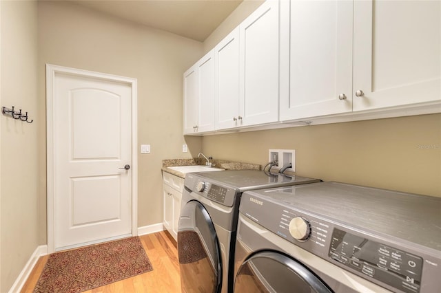 washroom featuring baseboards, light wood finished floors, a sink, washing machine and clothes dryer, and cabinet space