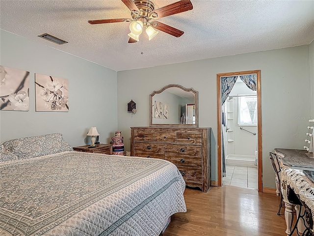 bedroom featuring a ceiling fan, a textured ceiling, visible vents, wood finished floors, and connected bathroom