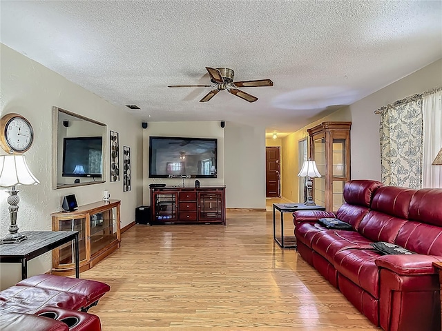 living room featuring visible vents, light wood-style floors, baseboards, a textured ceiling, and a ceiling fan