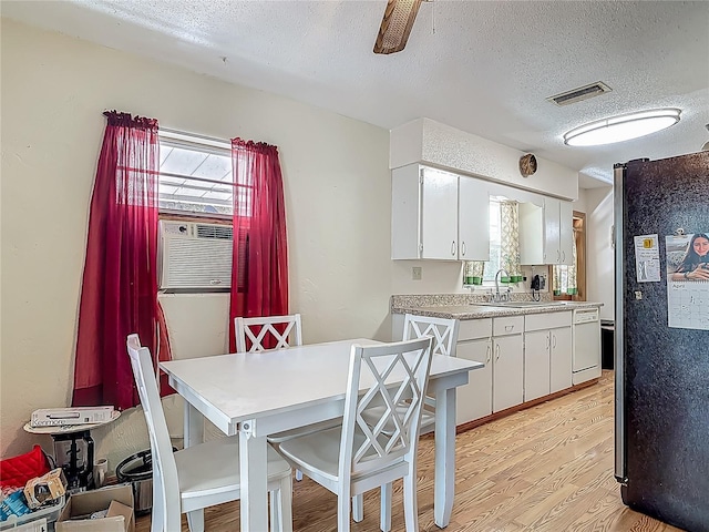 kitchen with a textured ceiling, light wood-type flooring, a sink, white cabinets, and freestanding refrigerator
