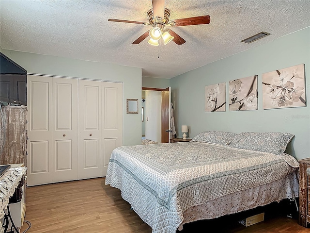 bedroom with a closet, a textured ceiling, wood finished floors, and visible vents