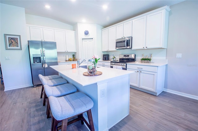 kitchen with appliances with stainless steel finishes, a sink, a breakfast bar area, wood finished floors, and a center island with sink