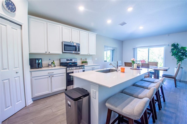 kitchen featuring appliances with stainless steel finishes, a sink, a breakfast bar area, recessed lighting, and light wood-type flooring