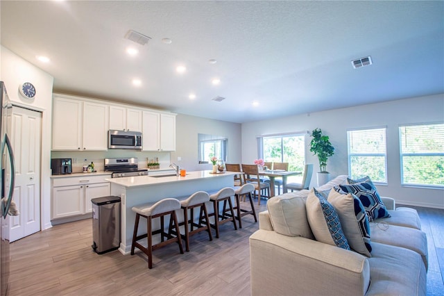 kitchen with visible vents, open floor plan, a breakfast bar area, a sink, and stainless steel appliances