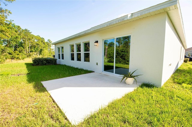 rear view of property featuring a yard, a patio, and stucco siding